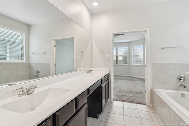 bathroom with tile patterned floors, plenty of natural light, a relaxing tiled tub, and vanity