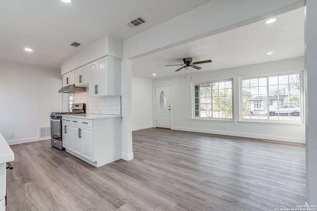 kitchen featuring stainless steel gas stove, light wood-type flooring, backsplash, ceiling fan, and white cabinets