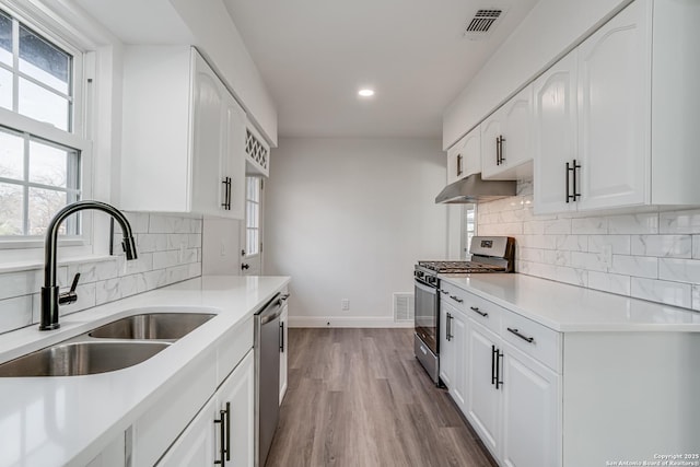 kitchen featuring sink, wood-type flooring, white cabinets, stainless steel appliances, and backsplash