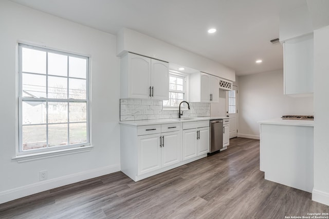 kitchen with tasteful backsplash, white cabinetry, dishwasher, sink, and light wood-type flooring