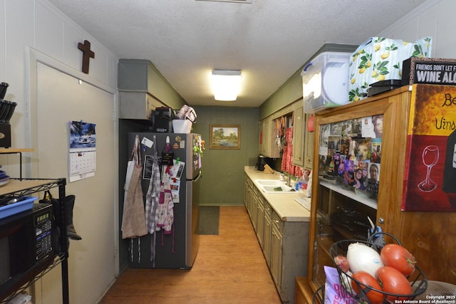 kitchen featuring stainless steel fridge, sink, a textured ceiling, and light wood-type flooring