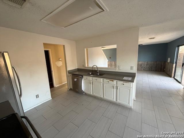 kitchen featuring sink, stainless steel dishwasher, a textured ceiling, fridge, and white cabinetry