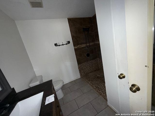 bathroom featuring tile patterned flooring, toilet, and tiled shower