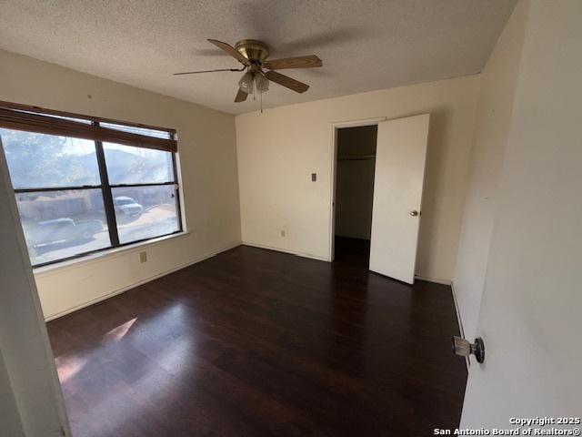 empty room with a textured ceiling, ceiling fan, and dark wood-type flooring