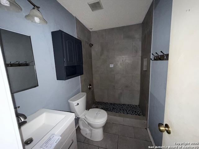 bathroom featuring tile patterned floors, vanity, toilet, and tiled shower