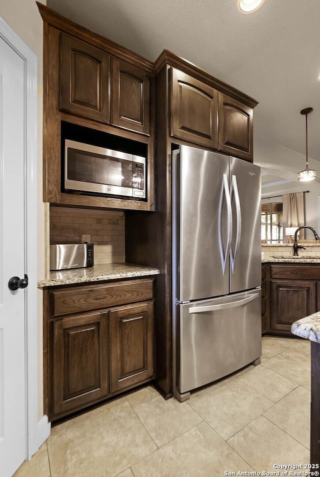 kitchen featuring appliances with stainless steel finishes, backsplash, dark brown cabinetry, sink, and pendant lighting