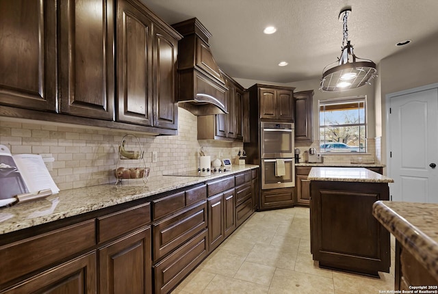 kitchen with light stone countertops, double oven, decorative light fixtures, decorative backsplash, and dark brown cabinets