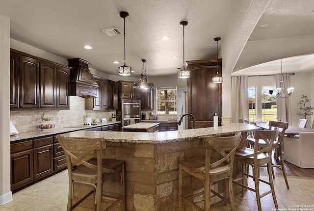 kitchen with a kitchen bar, light stone counters, dark brown cabinets, a large island with sink, and hanging light fixtures