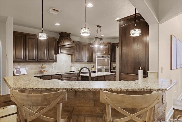 kitchen featuring a kitchen bar, light stone countertops, backsplash, custom range hood, and black electric cooktop