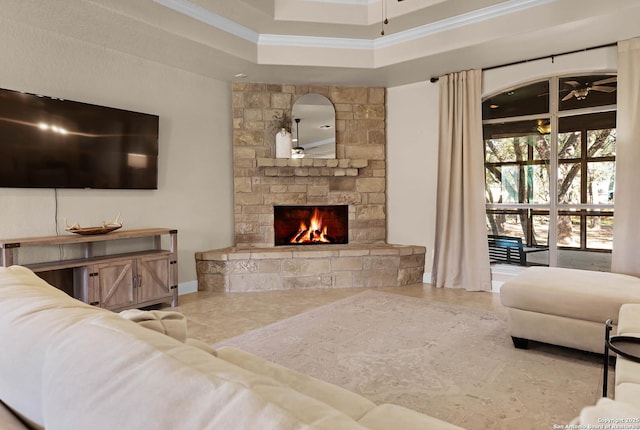 living room featuring a tray ceiling, a stone fireplace, ceiling fan, and ornamental molding