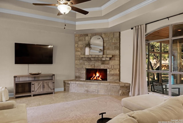 tiled living room with a raised ceiling, a stone fireplace, ceiling fan, and ornamental molding