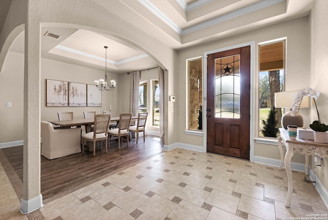 foyer entrance with a tray ceiling, an inviting chandelier, and ornamental molding