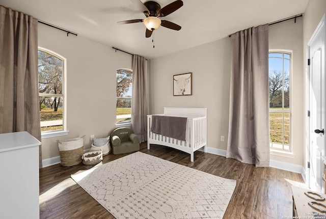 bedroom with multiple windows, dark hardwood / wood-style flooring, a nursery area, and ceiling fan