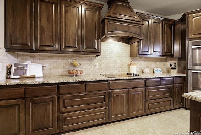 kitchen with multiple ovens, light stone counters, backsplash, black electric stovetop, and dark brown cabinets