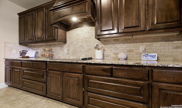 kitchen with decorative backsplash, light stone counters, custom exhaust hood, black electric cooktop, and light tile patterned flooring