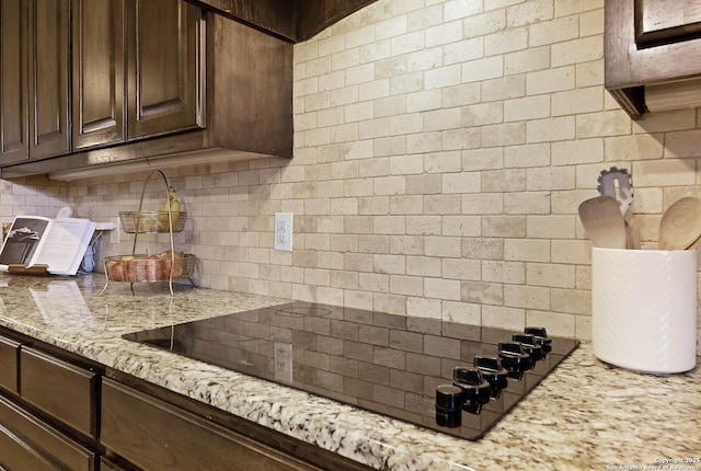 kitchen with black electric stovetop, light stone countertops, dark brown cabinetry, and backsplash