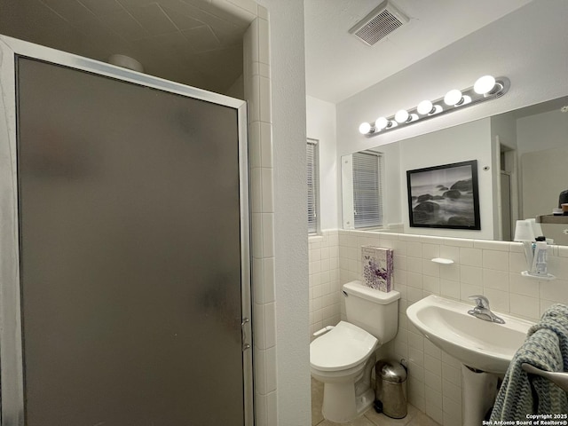 bathroom featuring toilet, a shower with shower door, and tile walls