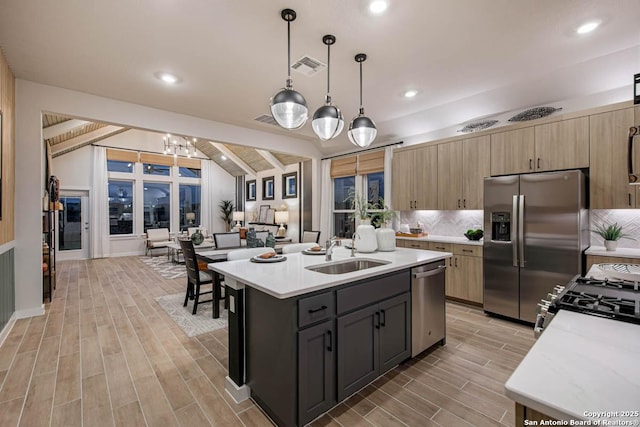 kitchen featuring appliances with stainless steel finishes, sink, lofted ceiling with beams, hanging light fixtures, and an island with sink