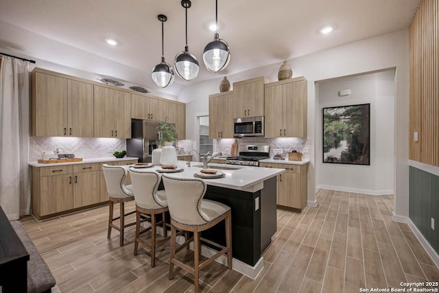 kitchen with hanging light fixtures, a kitchen breakfast bar, light brown cabinetry, a center island with sink, and appliances with stainless steel finishes