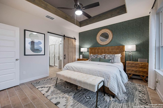 bedroom with ceiling fan, a barn door, and a raised ceiling