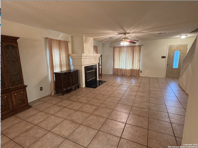 unfurnished living room featuring ceiling fan, light tile patterned floors, and a textured ceiling