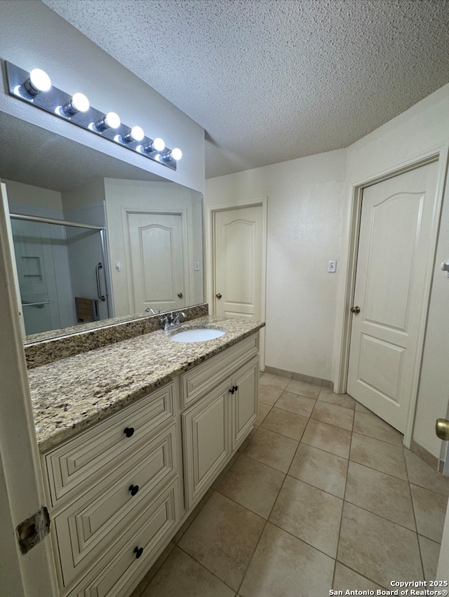 bathroom with vanity, a textured ceiling, tile patterned floors, and a shower with shower door