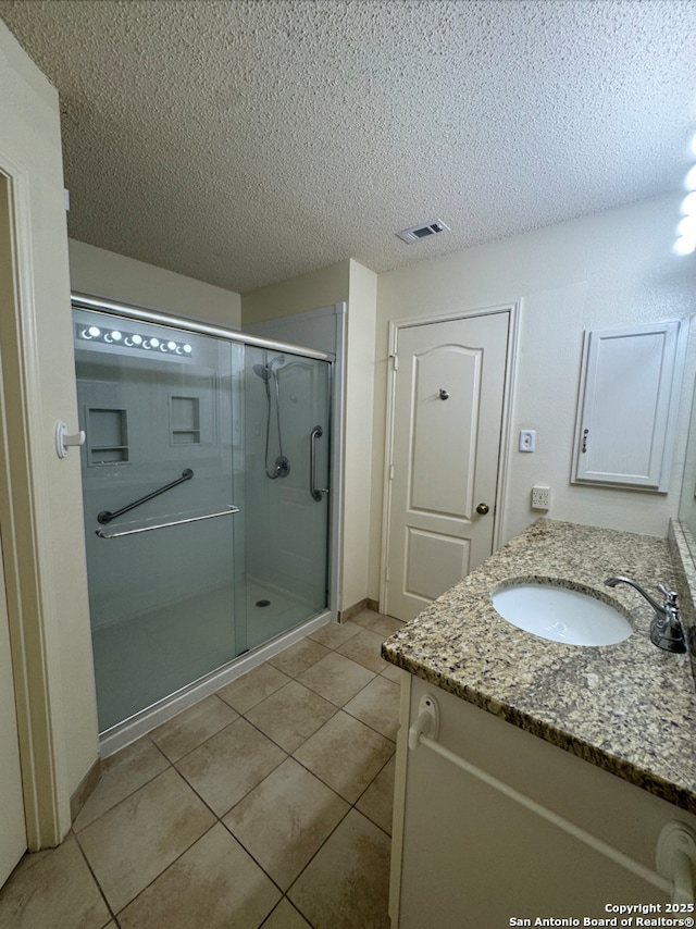 bathroom featuring tile patterned floors, a shower with door, vanity, and a textured ceiling