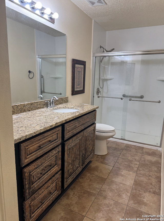 bathroom with toilet, vanity, a textured ceiling, and walk in shower