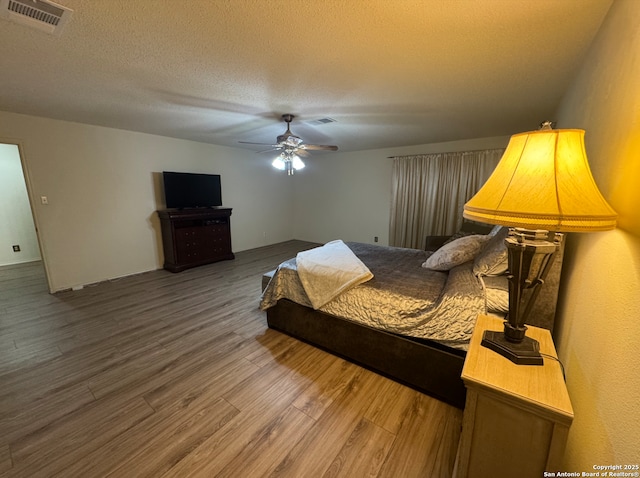 bedroom with ceiling fan, wood-type flooring, and a textured ceiling