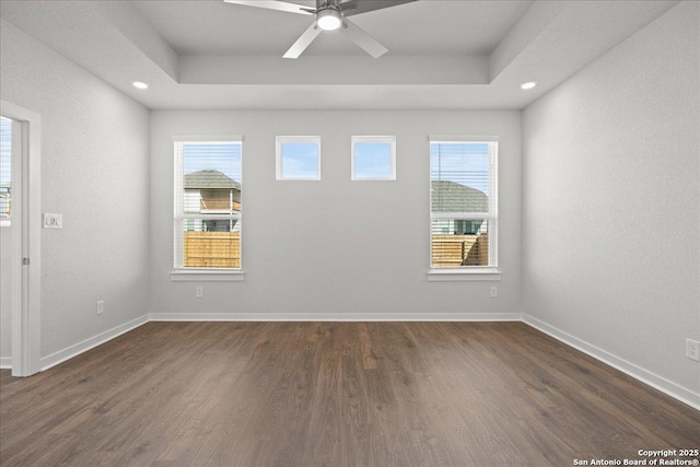 unfurnished room with a raised ceiling, ceiling fan, a healthy amount of sunlight, and dark hardwood / wood-style floors