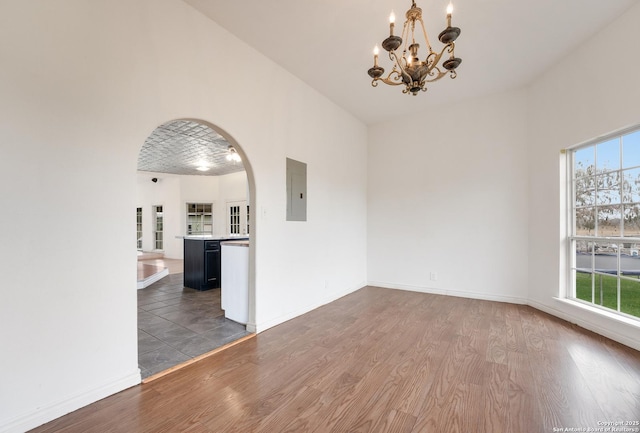 empty room featuring a notable chandelier, a wealth of natural light, dark hardwood / wood-style flooring, and electric panel