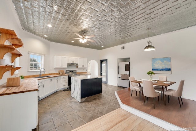 kitchen with wood counters, sink, stainless steel electric range oven, decorative light fixtures, and white cabinetry