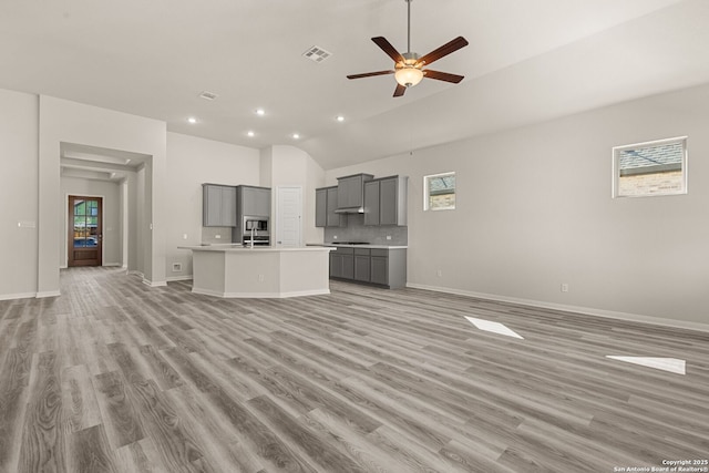 unfurnished living room with ceiling fan, vaulted ceiling, and light wood-type flooring