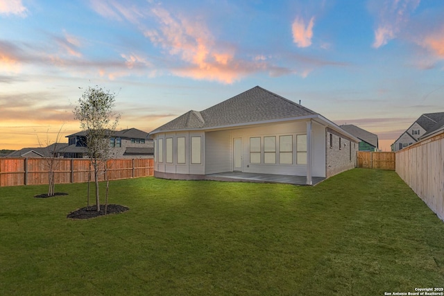 back house at dusk with a patio and a lawn