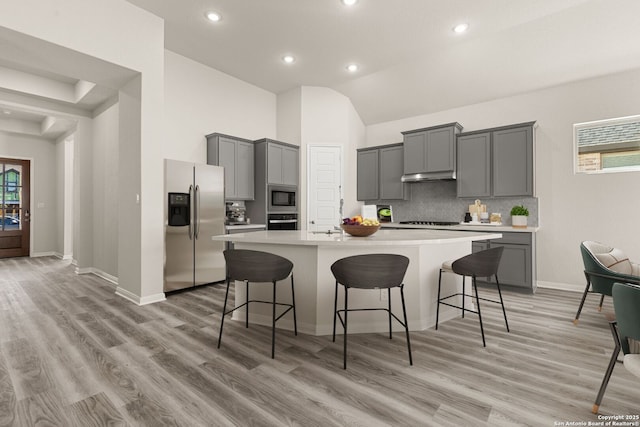 kitchen featuring light hardwood / wood-style flooring, gray cabinets, black appliances, an island with sink, and a kitchen bar