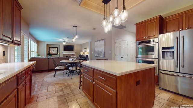 kitchen with ceiling fan, a kitchen island, stainless steel appliances, and hanging light fixtures