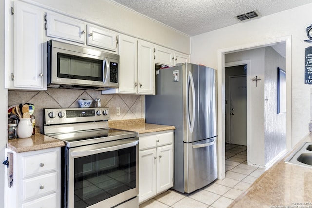 kitchen featuring stainless steel appliances, light tile patterned floors, backsplash, a textured ceiling, and white cabinets