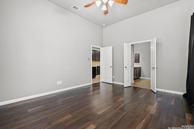 unfurnished bedroom with a towering ceiling, dark hardwood / wood-style flooring, connected bathroom, and ceiling fan