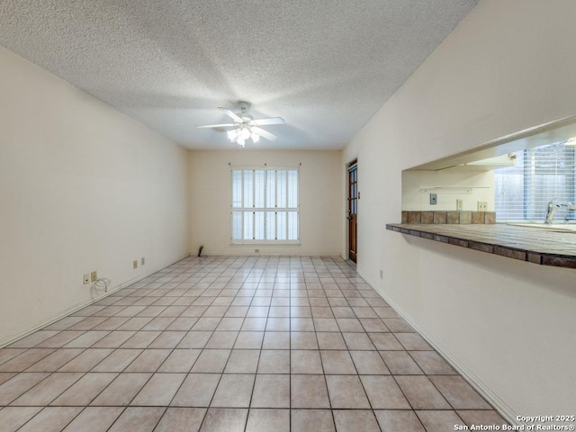 empty room with sink, light tile patterned floors, a textured ceiling, and ceiling fan