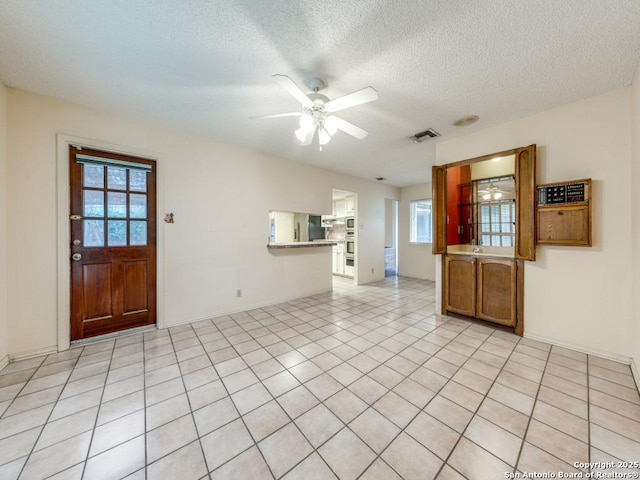 unfurnished living room with ceiling fan, light tile patterned floors, and a textured ceiling