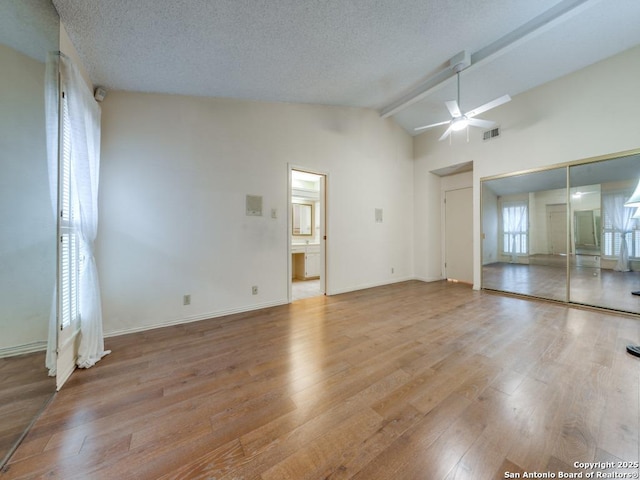 unfurnished living room featuring ceiling fan, lofted ceiling with beams, a textured ceiling, and light wood-type flooring