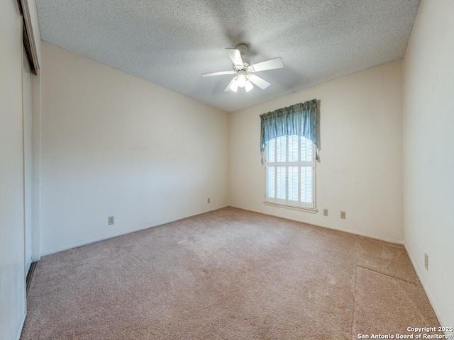 spare room featuring ceiling fan, light colored carpet, and a textured ceiling