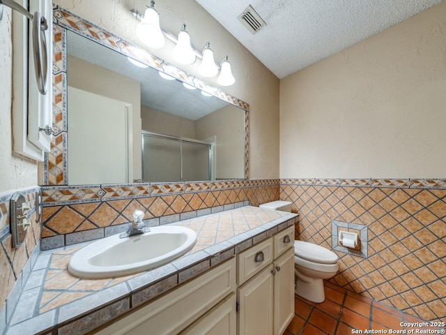 bathroom with toilet, an enclosed shower, a textured ceiling, tile walls, and vanity