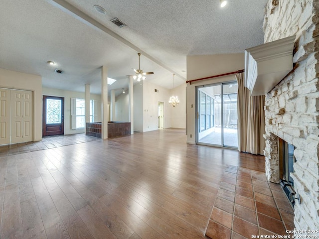 unfurnished living room featuring ceiling fan with notable chandelier, vaulted ceiling with beams, hardwood / wood-style floors, a textured ceiling, and a stone fireplace