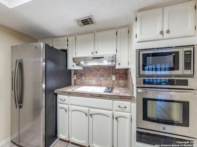 kitchen with tasteful backsplash, appliances with stainless steel finishes, white cabinets, and a textured ceiling