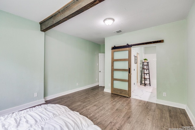 unfurnished bedroom with beam ceiling, a barn door, and hardwood / wood-style floors