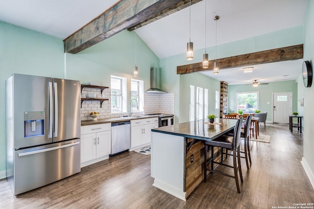 kitchen with white cabinetry, wall chimney exhaust hood, decorative light fixtures, a kitchen island, and appliances with stainless steel finishes