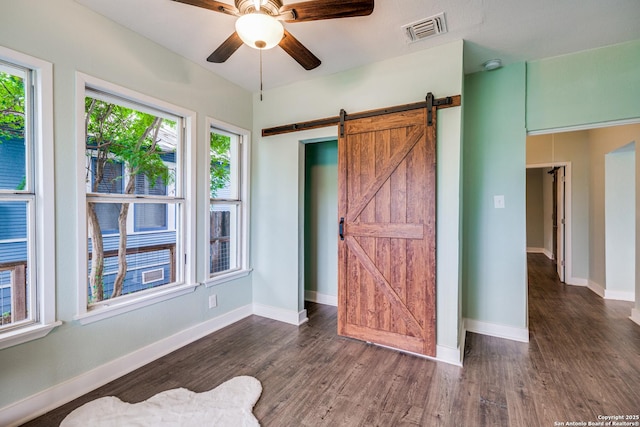 bedroom with a barn door, ceiling fan, and dark hardwood / wood-style floors