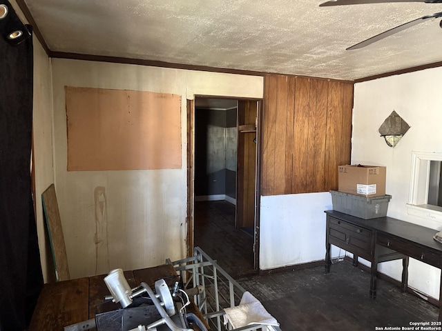 miscellaneous room featuring ceiling fan, wood walls, crown molding, and a textured ceiling