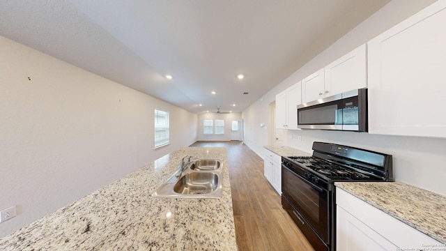 kitchen with light stone countertops, light wood-type flooring, black gas range oven, sink, and white cabinetry